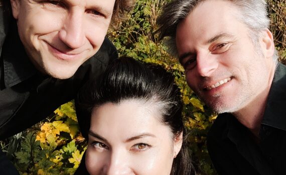 Die drei Musiker*innen von Pocket Tunes lachen vor einer Hecke in die Kamera.