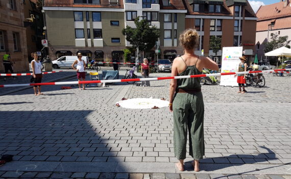 Menschen stehen im Keis auf dem Grünen Markt, in der Mitte liegt ein Tuch.